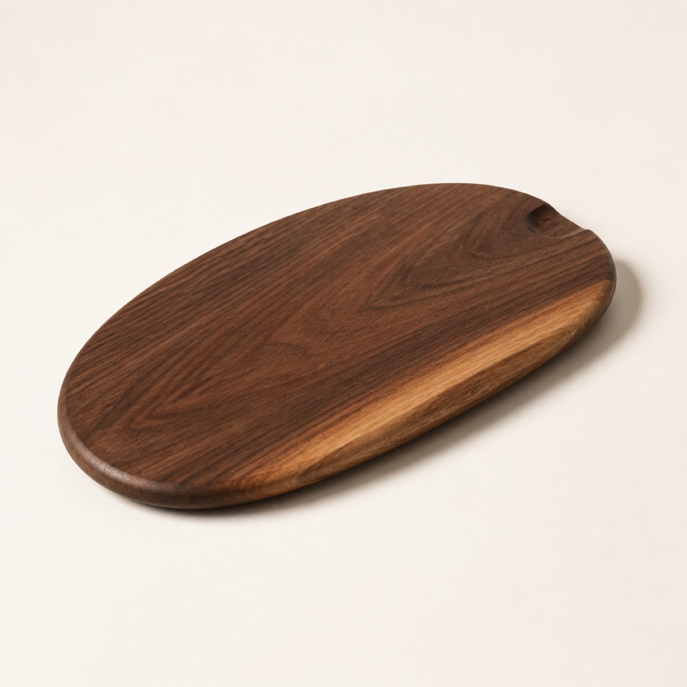 An oval hand-turned walnut serving board with a carved finger notch